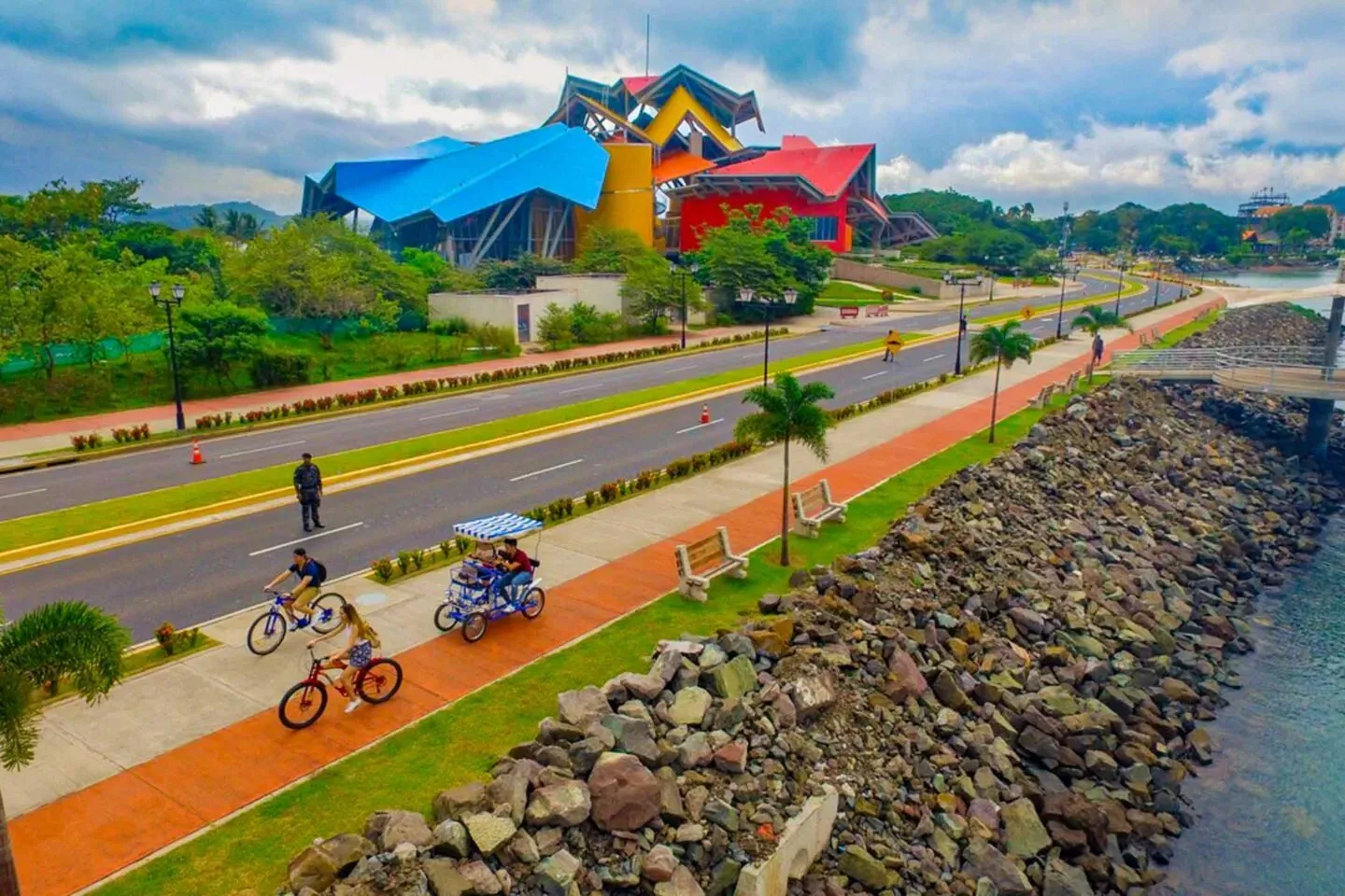 Cyclists riding the red waterfront path beside Biomuseo
